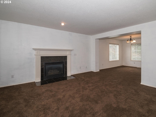 unfurnished living room with a tile fireplace, an inviting chandelier, a textured ceiling, and dark colored carpet