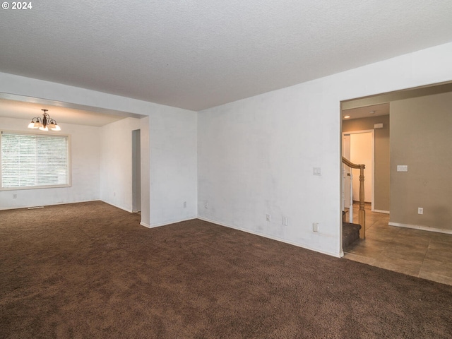 spare room featuring dark colored carpet, a textured ceiling, and a chandelier