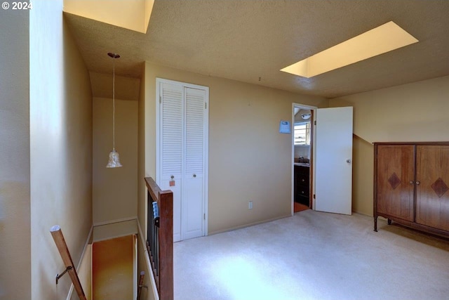 unfurnished bedroom featuring a skylight, a closet, light carpet, and a textured ceiling