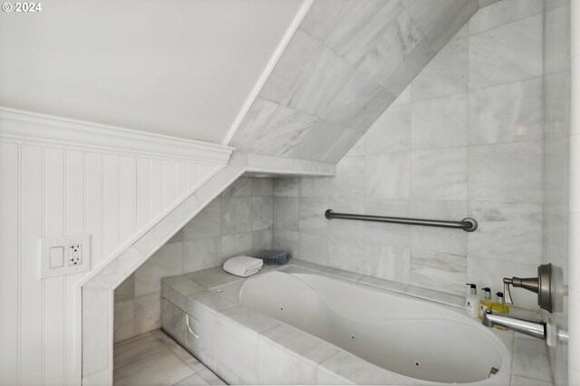 bathroom featuring tile walls, tiled tub, and vaulted ceiling