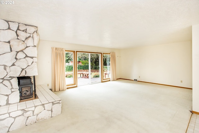 unfurnished living room featuring a textured ceiling, light colored carpet, and a wood stove