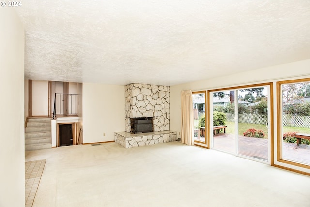 unfurnished living room with carpet, a stone fireplace, and a textured ceiling