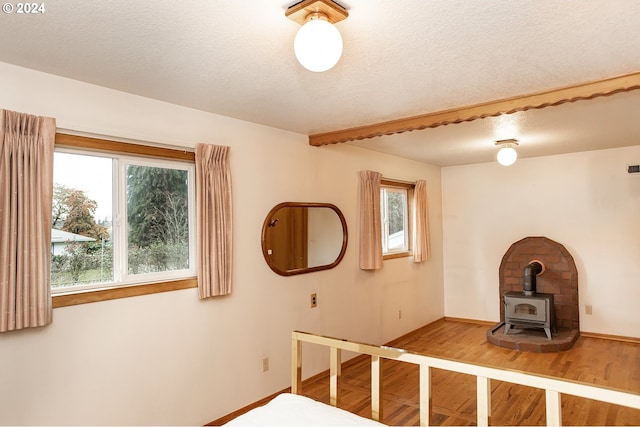 unfurnished bedroom with a textured ceiling, a wood stove, multiple windows, and hardwood / wood-style flooring