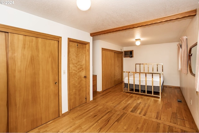 unfurnished bedroom featuring two closets, a textured ceiling, and light hardwood / wood-style floors