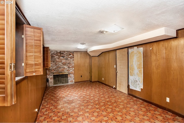 unfurnished living room featuring a textured ceiling, a brick fireplace, and wooden walls