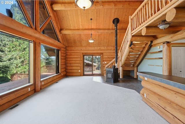 interior space with visible vents, wooden ceiling, a wood stove, dark colored carpet, and beam ceiling