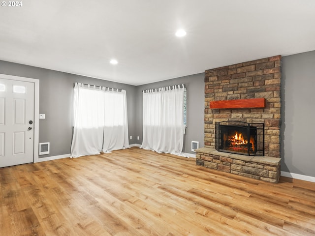 unfurnished living room featuring a stone fireplace and light wood-type flooring