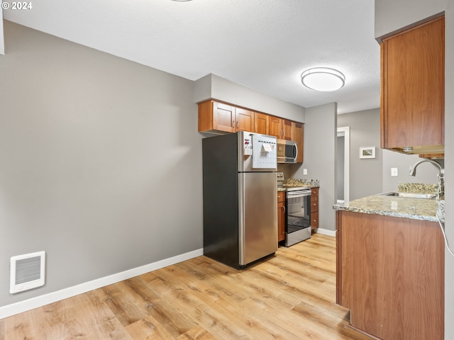 kitchen featuring light stone countertops, stainless steel appliances, light hardwood / wood-style floors, and sink