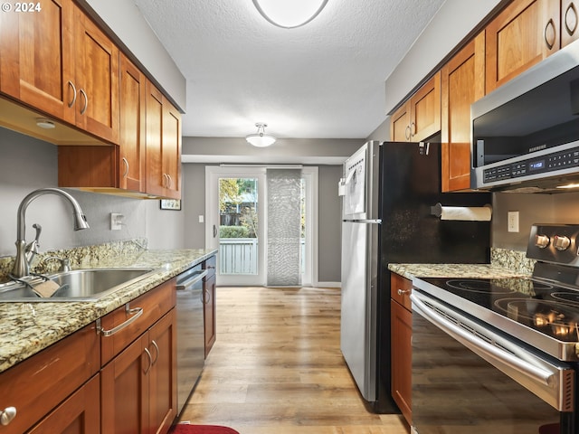 kitchen featuring sink, light wood-type flooring, a textured ceiling, light stone counters, and stainless steel appliances