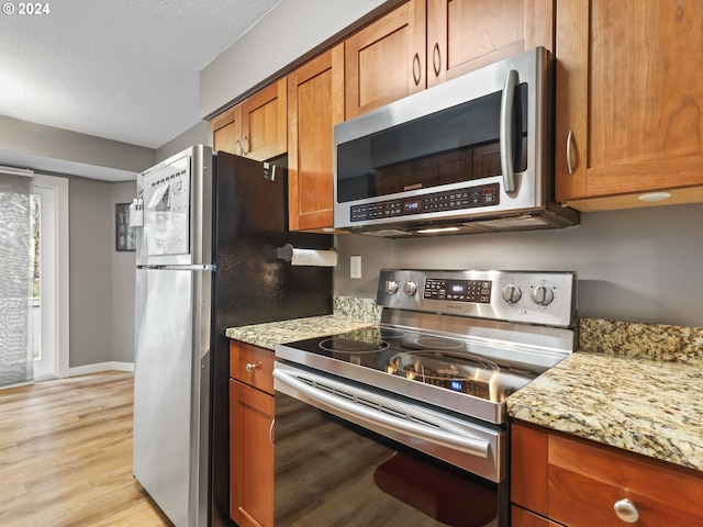 kitchen with a textured ceiling, light stone counters, stainless steel appliances, and light hardwood / wood-style flooring