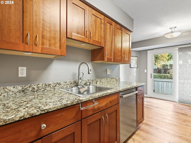 kitchen featuring sink, light stone counters, stainless steel dishwasher, a textured ceiling, and light wood-type flooring