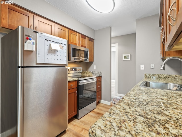 kitchen featuring appliances with stainless steel finishes, a textured ceiling, light hardwood / wood-style floors, and sink