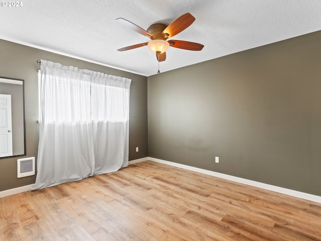 empty room with ceiling fan, light wood-type flooring, and a textured ceiling