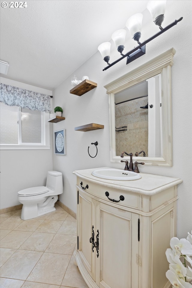 bathroom with tiled shower, tile patterned flooring, vanity, and toilet