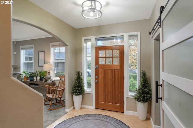 entryway featuring a barn door, crown molding, light hardwood / wood-style floors, and a textured ceiling