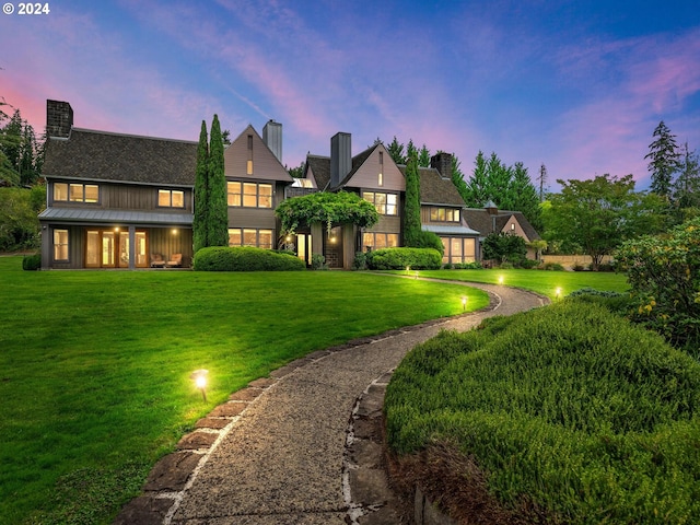 back of house at dusk featuring a standing seam roof, metal roof, and a lawn