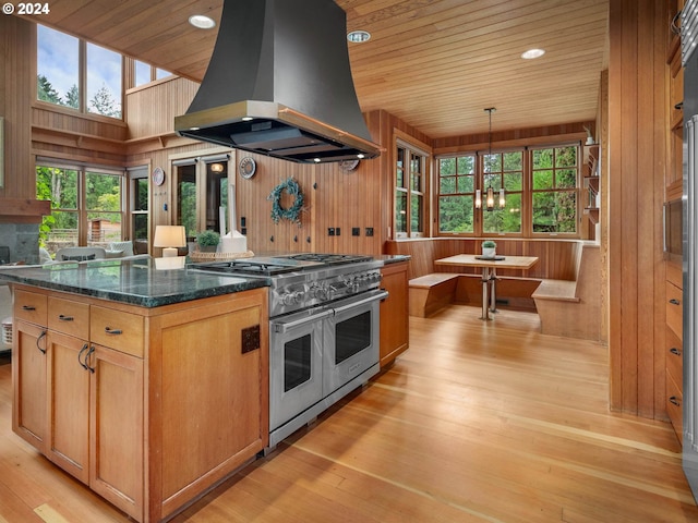 kitchen with range with two ovens, wood walls, a chandelier, light wood-type flooring, and island exhaust hood