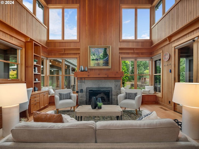 living room with light wood-type flooring, wooden walls, a healthy amount of sunlight, and a towering ceiling