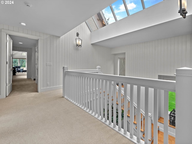 hall with a skylight, light carpet, and wooden walls