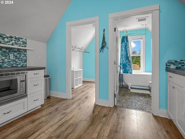 interior space with a bathing tub, vaulted ceiling, vanity, and wood-type flooring