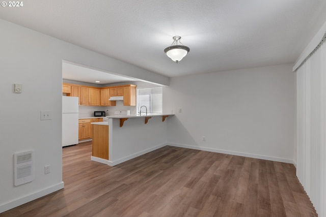 kitchen featuring a kitchen bar, light brown cabinetry, sink, white refrigerator, and kitchen peninsula