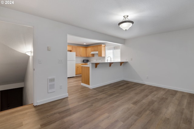 kitchen with a breakfast bar, light brown cabinetry, sink, white refrigerator, and kitchen peninsula