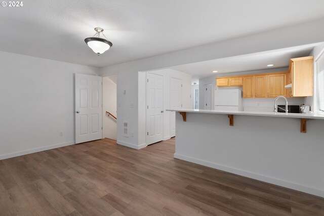 kitchen with light brown cabinets, dark hardwood / wood-style floors, a kitchen breakfast bar, kitchen peninsula, and white fridge