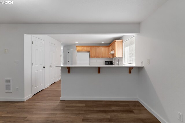 kitchen featuring a kitchen breakfast bar, light brown cabinets, dark hardwood / wood-style flooring, kitchen peninsula, and white fridge