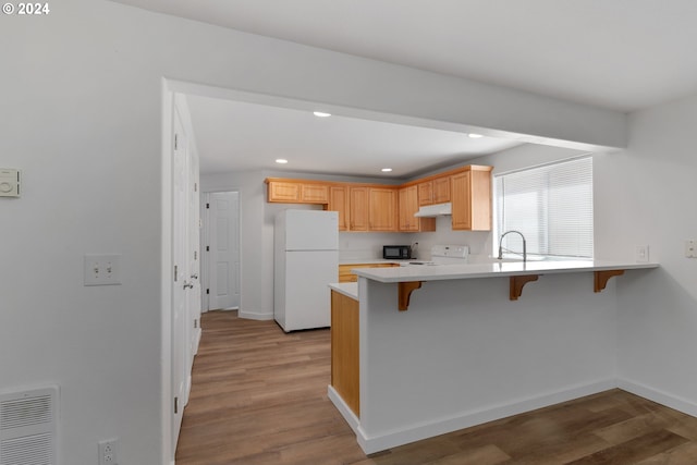 kitchen with light brown cabinetry, a breakfast bar, light wood-type flooring, kitchen peninsula, and white appliances