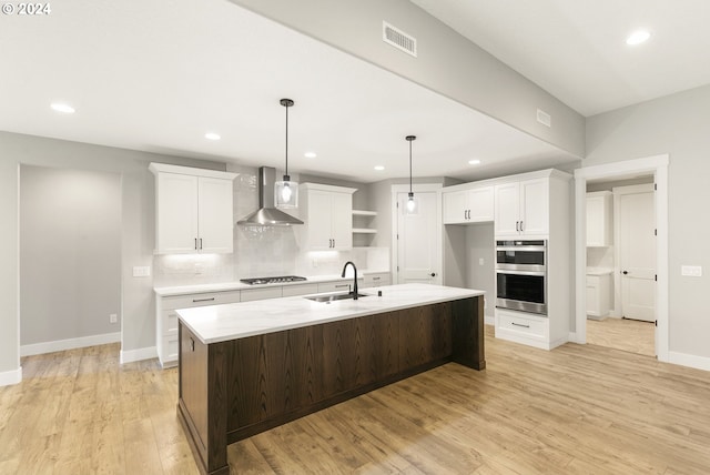 kitchen with a center island with sink, light hardwood / wood-style flooring, wall chimney range hood, and white cabinets