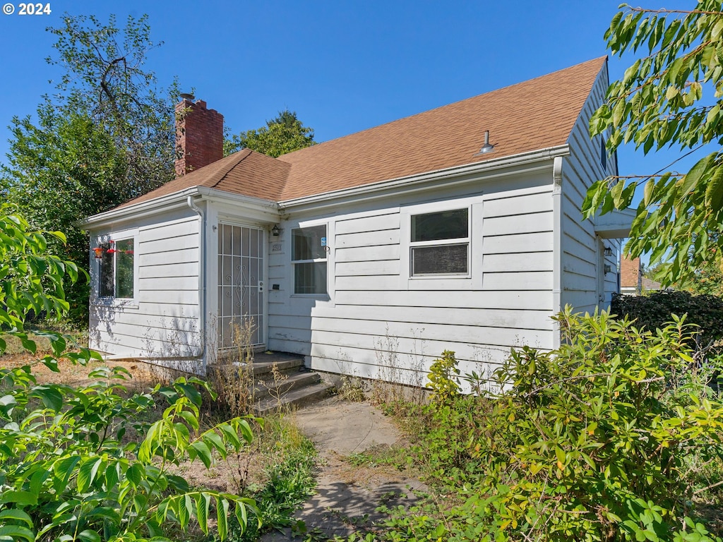 back of house featuring roof with shingles and a chimney