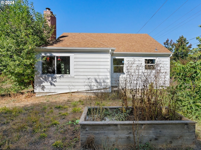 back of house featuring a shingled roof, a chimney, and a vegetable garden