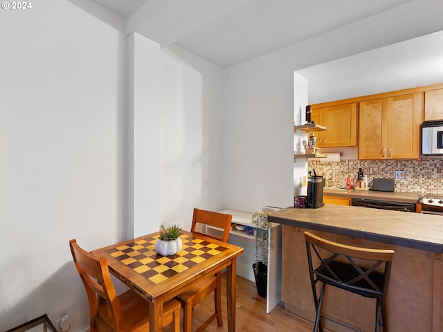 kitchen with tasteful backsplash, dishwasher, light hardwood / wood-style flooring, a breakfast bar, and tile countertops