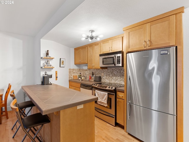 kitchen featuring light brown cabinetry, appliances with stainless steel finishes, light wood-type flooring, tile countertops, and a breakfast bar