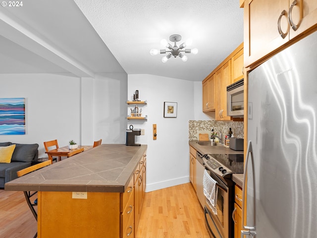 kitchen with a kitchen bar, tile counters, appliances with stainless steel finishes, light wood-type flooring, and kitchen peninsula