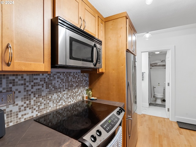 kitchen featuring decorative backsplash, light hardwood / wood-style floors, a textured ceiling, and appliances with stainless steel finishes