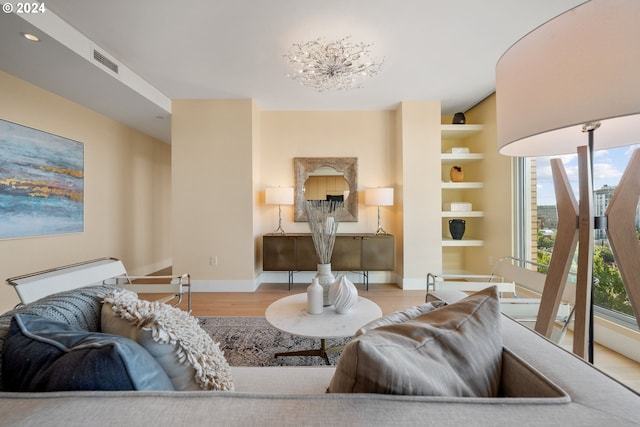 living room featuring built in shelves, a chandelier, and light hardwood / wood-style flooring