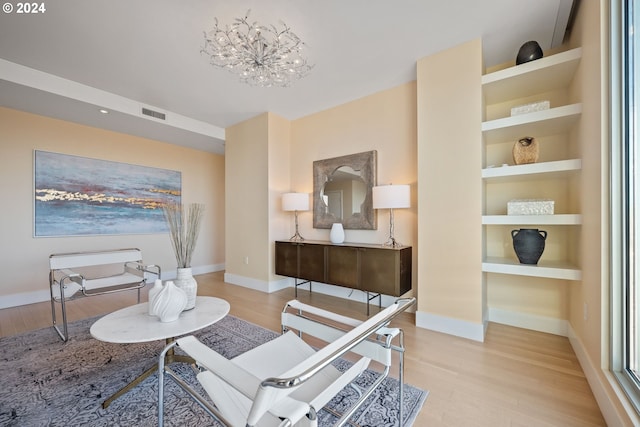 sitting room with built in features, a notable chandelier, and light hardwood / wood-style floors