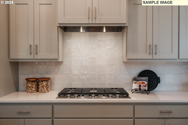 kitchen with decorative backsplash, gray cabinets, light countertops, wall chimney range hood, and stainless steel gas cooktop