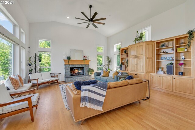 living room with light hardwood / wood-style floors, a stone fireplace, high vaulted ceiling, and ceiling fan