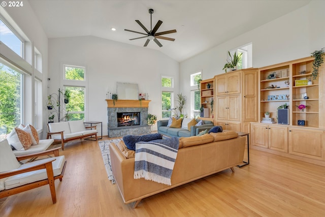 living room with ceiling fan, a stone fireplace, high vaulted ceiling, and light hardwood / wood-style flooring