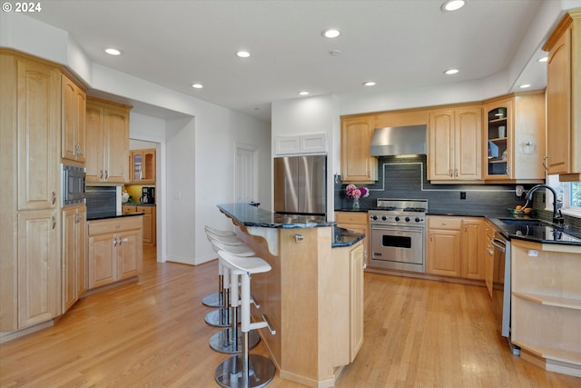 kitchen featuring stainless steel appliances, wall chimney exhaust hood, sink, a center island, and light hardwood / wood-style flooring