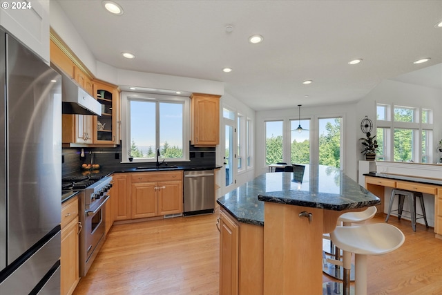 kitchen with stainless steel appliances, sink, backsplash, a kitchen island, and wall chimney exhaust hood