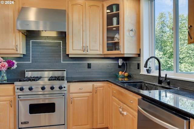 kitchen featuring sink, appliances with stainless steel finishes, range hood, light brown cabinetry, and dark stone counters