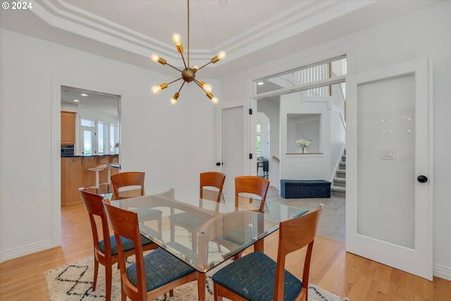 dining space featuring an inviting chandelier, a raised ceiling, and light hardwood / wood-style flooring