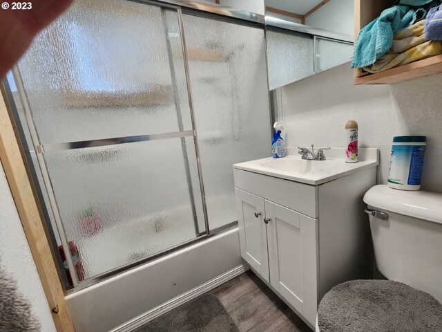 full bathroom with hardwood / wood-style flooring, vanity, toilet, and bath / shower combo with glass door