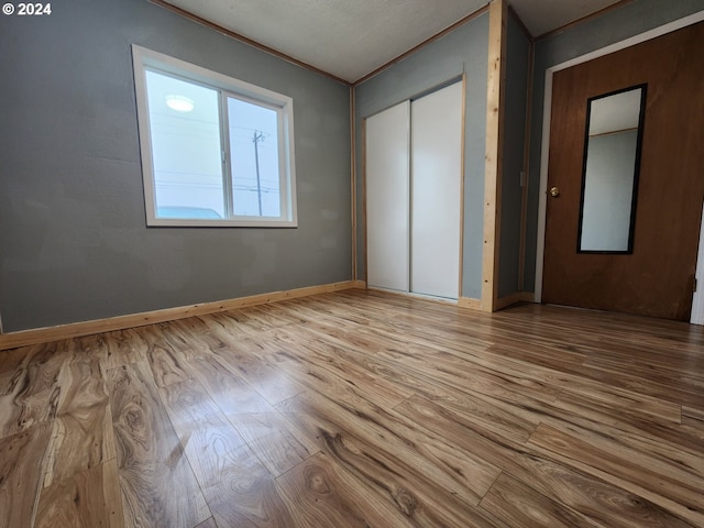 unfurnished bedroom featuring hardwood / wood-style flooring, crown molding, and a closet