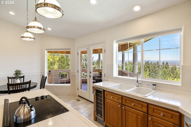 kitchen featuring tile countertops, light tile patterned floors, beverage cooler, black cooktop, and sink