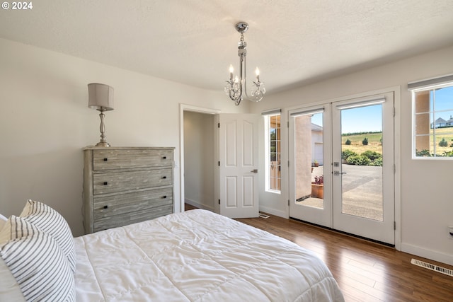 bedroom with a textured ceiling, a notable chandelier, french doors, dark hardwood / wood-style flooring, and access to exterior