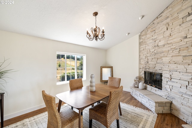 dining space featuring light hardwood / wood-style floors, a stone fireplace, vaulted ceiling, and a chandelier